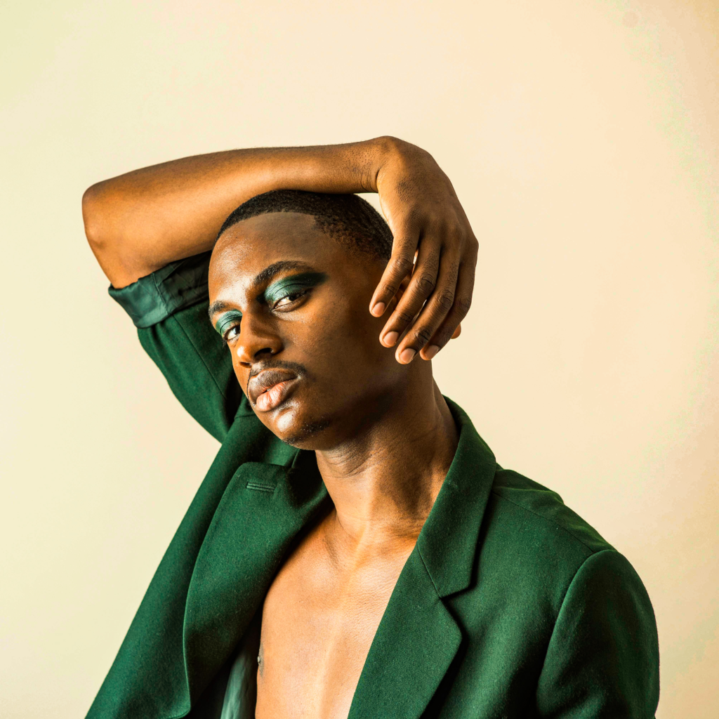 Male Gen-Z fashion model in green outfit with LGBTQ+ styling, retouched using Photoshop dodge & burn, frequency separation, and cyber-luxe gradient maps for inclusive editorial clarity.