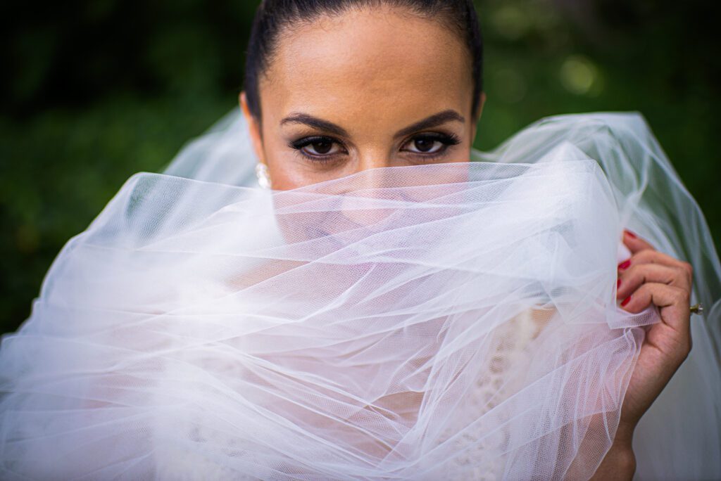 “Bride hiding her face with veil, retouched using Photoshop dodge & burn, frequency separation, and golden hour LUTs for cinematic softness and romantic mystery.