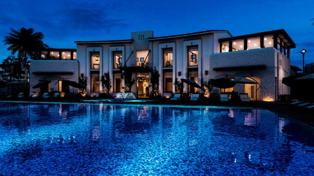 Dusk view of a blue resort pool with illuminated deck, loungers, and reflective water — la noir’e Da Vinci retouch.